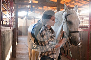 Female farmer standing with white horse at stabling indoor