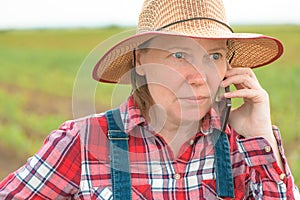 Female farmer talking on mobile phone in young green corn field