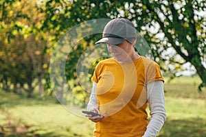 Female farmer using smartphone in walnut tree orchard. Farm worker wearing orange t-shirt and trucker`s hat with mobile phone in