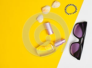 Female fashion accessories on a yellow white pastel background. Sunglasses, perfume bottle, shells. Summer beach accessories.