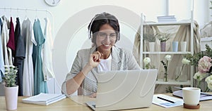 Female fashion designer wearing headphones making video call on laptop