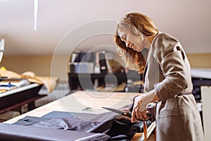 Female fashion designer working on suiting fabric with dressmaking accessories on table