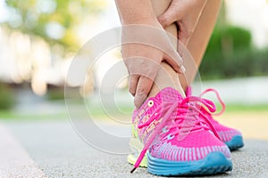 Female fatty runner athlete leg injury and pain. Hands grab painful ankle while running in the park