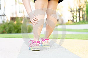 Female fatty runner athlete leg injury and pain. Hands grab painful leg while running in the park