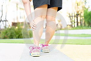 Female fatty runner athlete leg injury and pain. Hands grab painful leg while running in the park