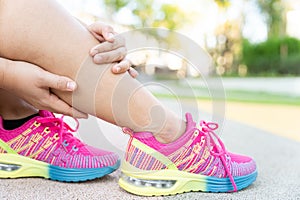 Female fatty runner athlete leg injury and pain. Hands grab painful leg while running in the park