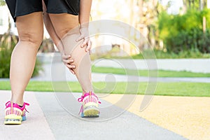 Female fatty runner athlete leg injury and pain. Hands grab painful leg while running in the park