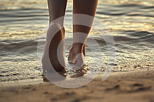 Female feet barefoot on a sandy beach in the water. Close-up of beautiful female legs. Wet foot