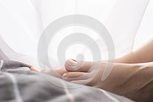 Female feet in bed. The bed is gray, pink, soft pastel colors.