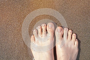 Female feet with beige nail design. Glitter beige nail polish pedicure on ocean beach sand. Summer vacation pedicure