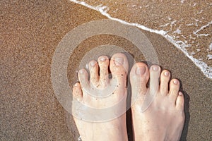 Female feet with beige nail design. Glitter beige nail polish pedicure on ocean beach sand. Summer vacation pedicure