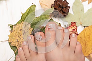 Female feet with beige nail polish. Woman legs with autumn nail design on wooden background with fallen leaves