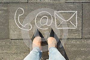 Female feet with contact symbols phone mail and letter, written on grey sidewalk, communication or contact us concept.