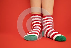 Female feet in fluffy New Year or Christmas warm socks. The colors of the socks are red and white stripes and green heels and tips