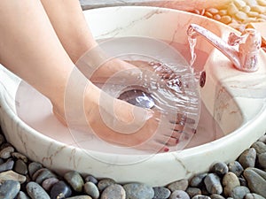 Female feet in foot spa marble basin with water flowing from faucet