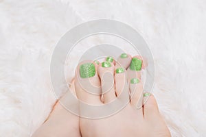 Female feet with green nail design. Glitter green nail polish pedicure on white fluffy background