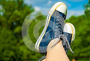 Female feet in jeans sneakers on the background of a sky and tree