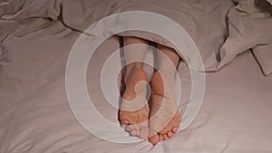 female feet move in their sleep at night under blanket on a white sheet. A woman girl sleeps on a bed in a hotel bedroom