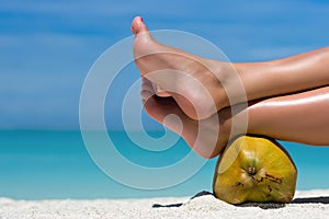 Female feet propped on coconut on the beach, blue sea background