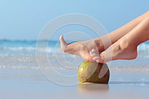 Female feet propped on coconut on sea background photo