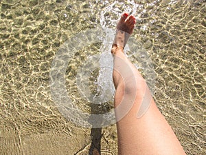 Female feet with red, coral pedicure steps into clear seawater. Vacation on the beach