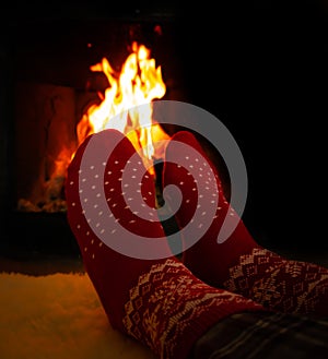 Female feet in red woolen socks by a warm fireplace on a cold winters evening