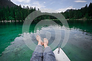 Female feet rest on boat at alpine mountain lake