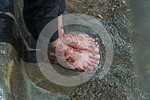 Female feet in the river Ganges water with henna tattoo, close up, India