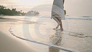 Female feet running barefoot on tropical sandy beach at summer sunset. Slim woman's legs run on sand, leaving