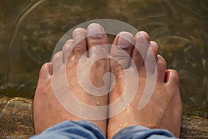 Female feet in running water. Close-up of female legs wearing jeans and resting while wetting her feet. LSG