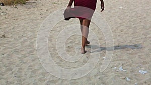 Female feet on the sand in a developing red dress. An