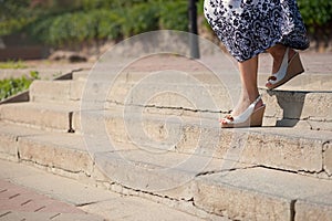 Female feet in sandals on the top of big steps down. Long pathway downstairs