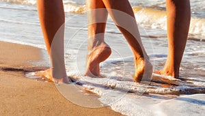 female feet on a sandy beach in the waves of the surf of the sea in summer close up