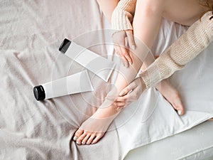 Female feet and skin care cream in tubes on the bed. Skin care concept