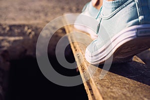 Female feet in sneakers walking on a narrow board above a large