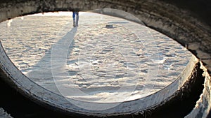 Female feet in sneakers walking on sea shore at sunset, view through tire