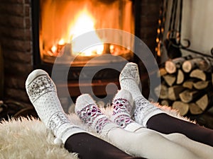 Female feet in soft wool socks and burning fire in fireplace at the background. Warming and unwinding near fireplace with a cup of