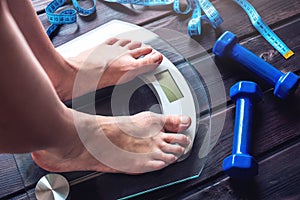 Female feet standing on electronic scales, dumbbells and measuring tape. Concept of slimming and weight loss