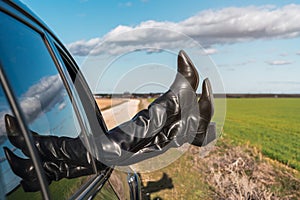 Female feet sticking out of a car window with a beautiful view of green fields under a blue sky with clouds