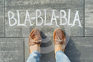 Female feet with text bla-bla-bla written on grey sidewalk