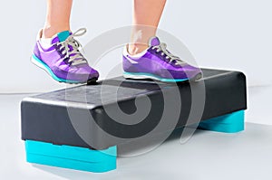 Female feet in violet sneakers on fitness aerobic step.