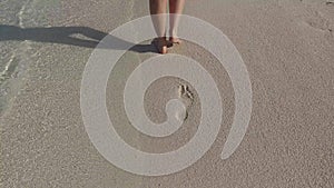 Female feet walking on sandy beach with footprints