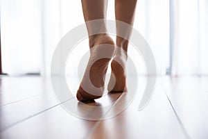 Female feet walks on warm laminate floor closeup rear view