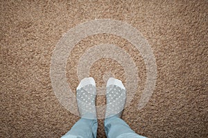 Female feet in warm socks against a background of brown carpet, space for text