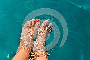 Female feet in the water, beautiful bright blue water, texture of the blue water surface