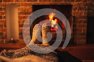 Female feet wearing white socks sitting near fireplace, wrapping in a woolen blanket