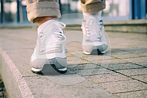 Female feet in white sneakers walking on the sidewalk