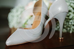 Female feet in white wedding sandals with a bouquet of camomiles