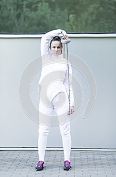 female fencer of millennial generation wears white fencing costume, holds metal epee above head
