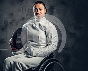 Female fencer in wheelchair holds safety mask and a sword.
